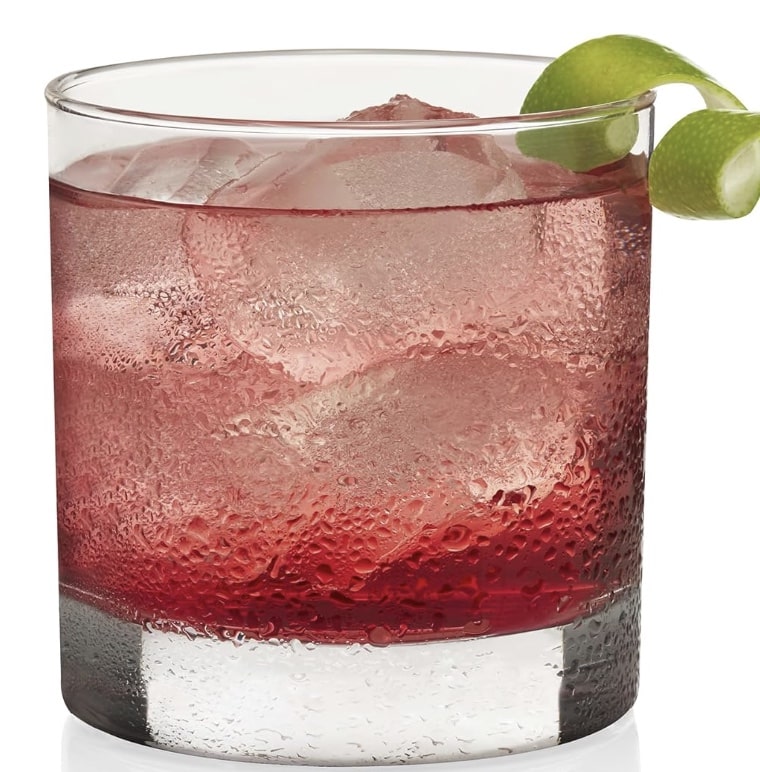 A glass filled with a red beverage and ice cubes, garnished with a twist of lime on the rim, makes for one of those easy summer mocktail recipes. The condensation on the glass suggests it's chilled.